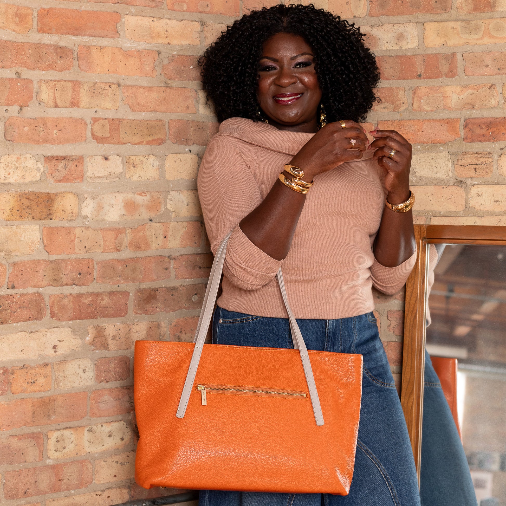 Woman holding an orange tote bag against a brick wall