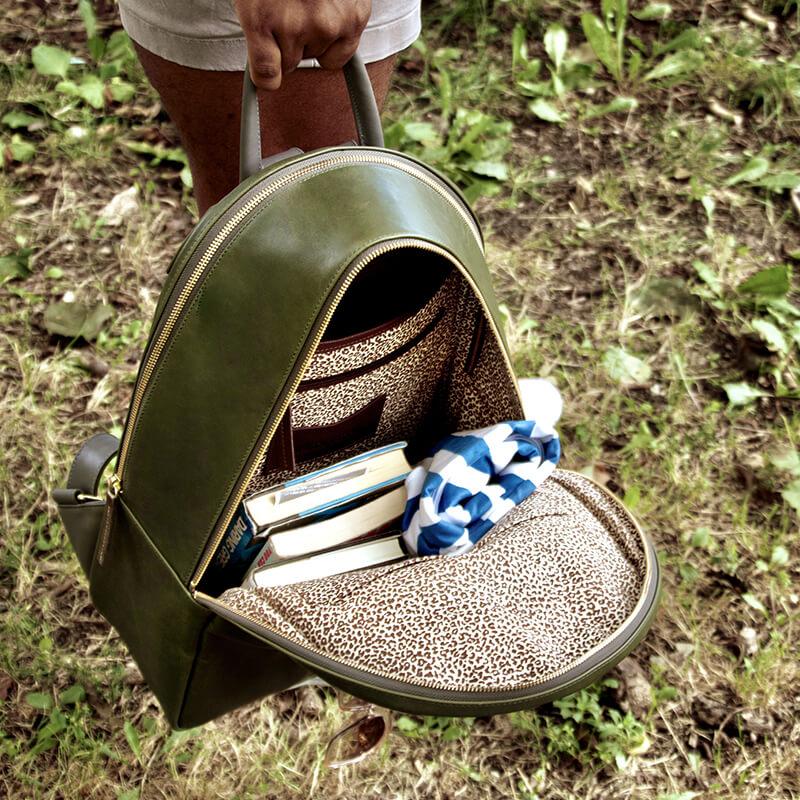 A man is holding open his Moto Large backpack. You can see the inside Brown Spotted cotton lining and a few books nestled inside.
