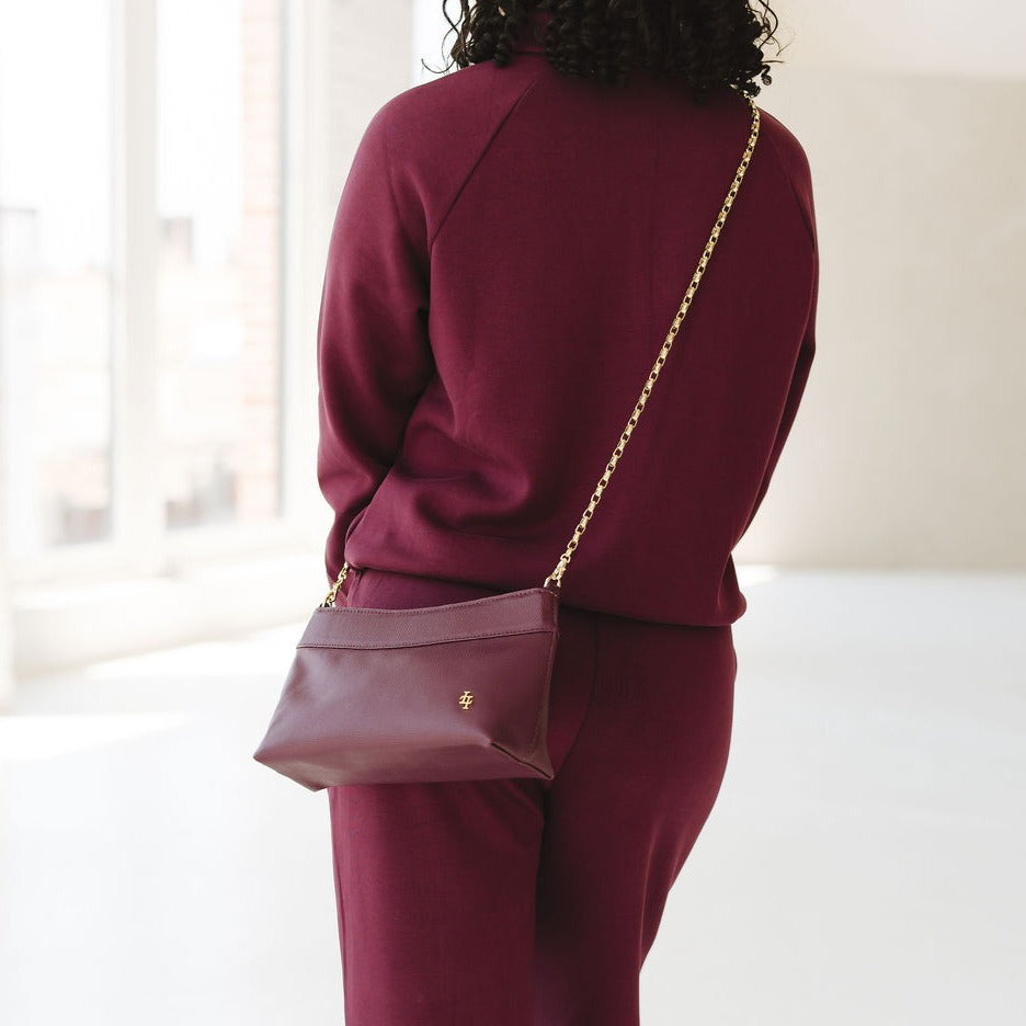 Person wearing a burgundy outfit with a matching handbag in a bright room.