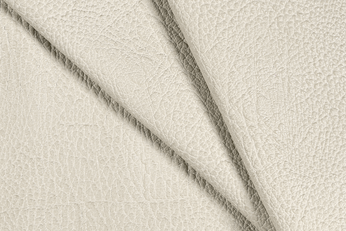 A close-up of textured cream-colored leather with a pebbled grain, folded diagonally to show the surface texture and color.
