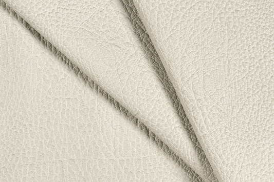 A close-up of textured cream-colored leather with a pebbled grain, folded diagonally to show the surface texture and color.