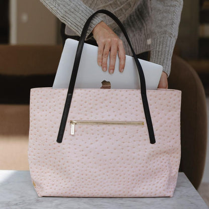 Pink textured handbag with black handles holding a white laptop on a marble surface.